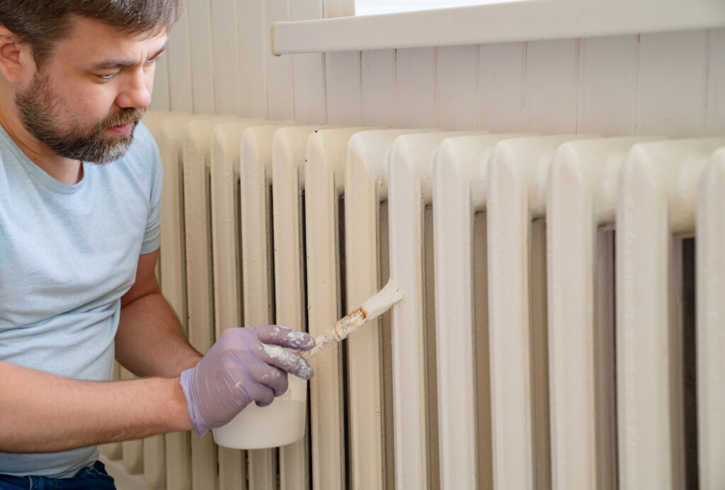 man in glove painting heating radiator in home